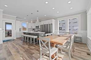 Una cocina moderna con armarios blancos, una isla grande con taburetes de bar y un comedor con mesa de madera y sillas blancas.