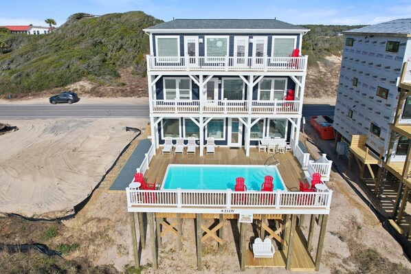 Una casa frente al mar de dos pisos con piscina, sillas de terraza y vistas a la playa.