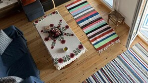 Una sala de estar acogedora con un sofá, una mesa de centro con camino de mesa floral y un tapete a rayas.