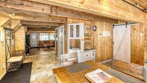 A wooden interior with a dining table, chairs, a kitchen area, and a staircase leading to another room.