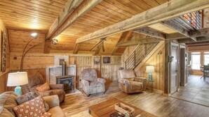 A cozy log cabin interior with a fireplace, leather sofas, and a staircase leading to an upper level.