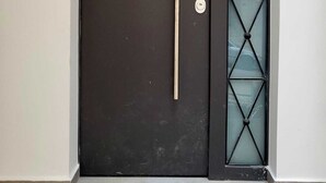 En mørk dør med et lodret håndtag og et glasfelt med et diamantmønster.