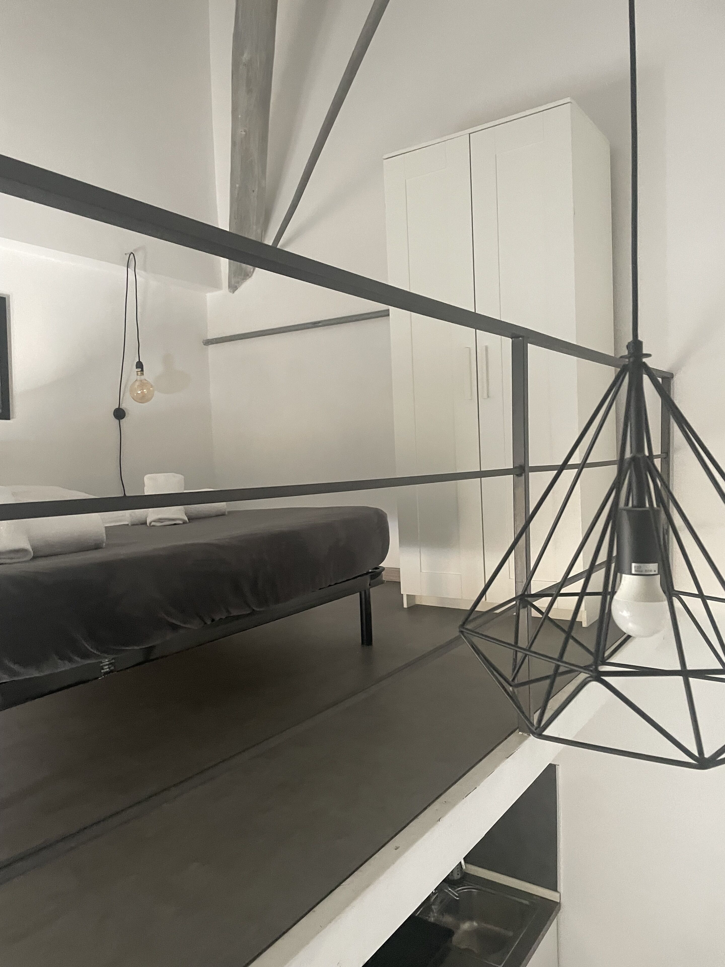 A modern, minimalist bedroom with a bed, a hanging light fixture, and a wardrobe.