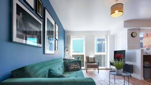 Ein modernes Wohnzimmer mit einem türkisfarbenen Sofa, gerahmten Kunstwerken an der Wand, einem Netflix-Schild und einem großen Fenster.