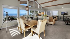 Amplia sala de estar con una mesa de comedor de madera, sillones cómodos y un gran ventanal con vistas al océano.