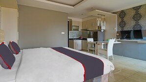A hotel room with a bed, a desk, and a kitchenette. - OYO Life 92774 The Edge Apartment By My Home (Cimahi)