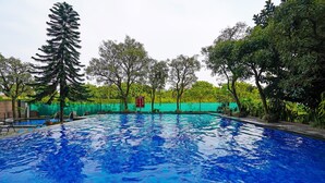 A swimming pool surrounded by trees and a green fence. - OYO Life 92774 The Edge Apartment By My Home (Cimahi)