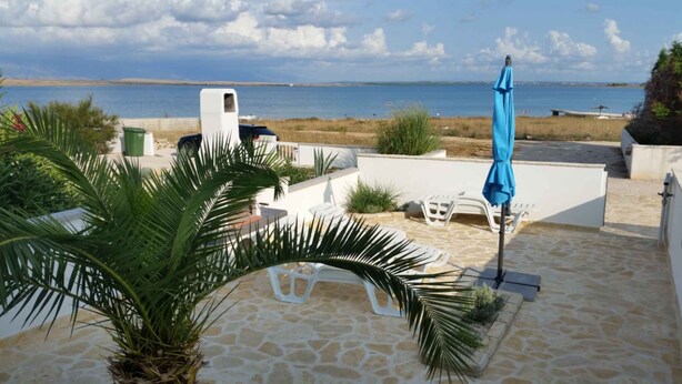 Una veranda con pavimento in pietra, mobili bianchi e un ombrellone blu.