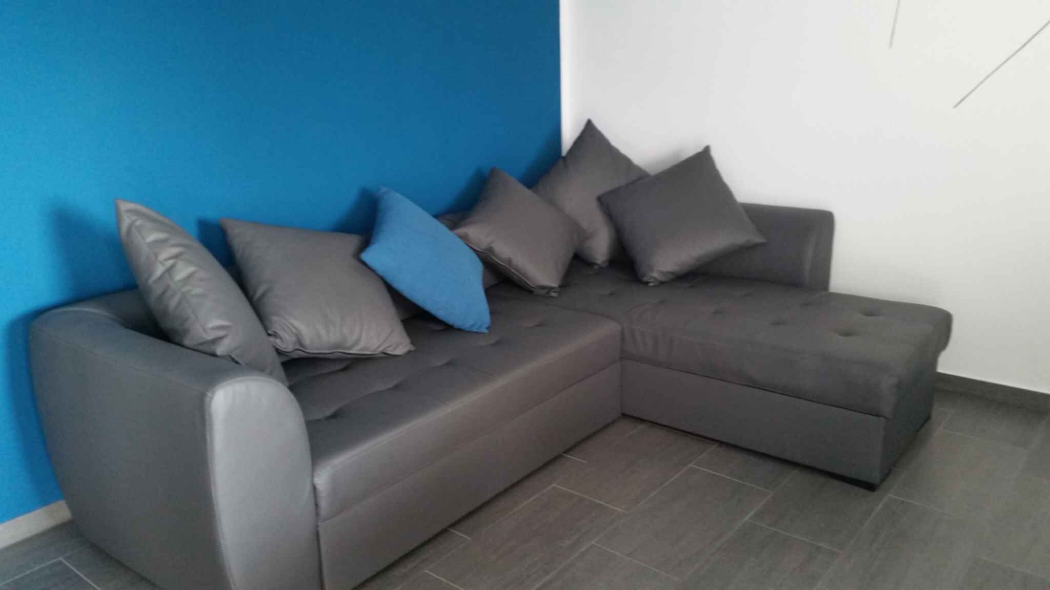 A grey sectional sofa with multiple cushions against a blue wall and a white wall.