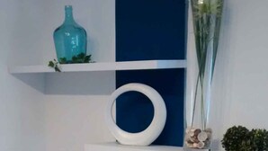 Ett modernt vardagsrum med en platt-TV placerad på en vit TV-bänk, en blå accentvägg och dekorativa föremål, inklusive en vas och en glasskål.