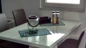 En matplats med ett glasbord, fyra stolar, en liten prydnadsföremål och ett fönster som släpper in naturligt ljus.