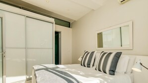 A bedroom with a bed, a bedside lamp, a mirror, and a sliding door. - Compact Camps Bay Holiday Apartment With Private Pool Sea Escape (Cape Town)