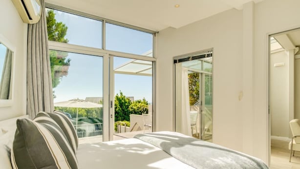 A bedroom with a large window, a bed, and a sliding glass door leading to an outdoor area. - Compact Camps Bay Holiday Apartment With Private Pool Sea Escape (Cape Town)