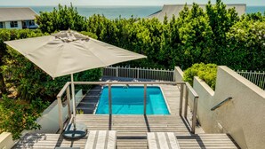 A wooden deck with a pool, surrounded by greenery and a view of the ocean. - Compact Camps Bay Holiday Apartment With Private Pool Sea Escape (Cape Town)