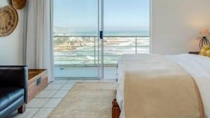 Une chambre dotée d’un grand lit, d’une commode, d’une table de chevet et offrant une vue sur l’océan grâce à une porte-fenêtre coulissante.