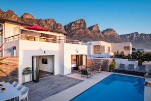 Une maison moderne à deux étages, dotée d’une piscine, d’une terrasse en bois et offrant une vue sur les montagnes.