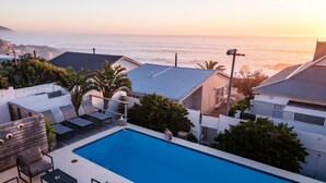 Une piscine sur le toit, dotée de chaises longues et offrant une vue sur l’océan au coucher du soleil.
