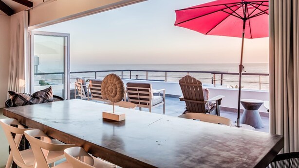 Une terrasse avec vue sur l’océan, un parasol rouge et des sièges confortables.