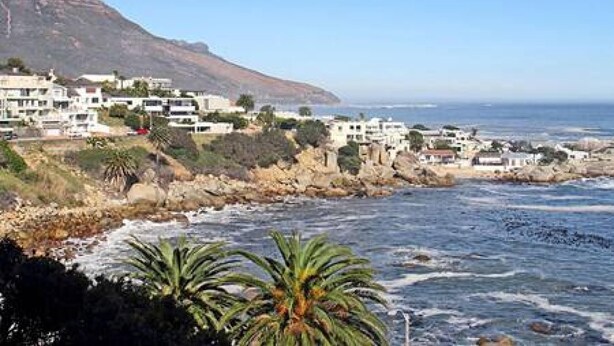 A coastal town with buildings along the shoreline, a prominent mountain in the background, and a view of the ocean. - Holiday Apartment w Sea Views Pool CBT Suite (Cape Town)