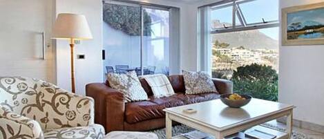 A modern living room with a brown leather sofa, patterned armchair, and a coffee table. A large window offers a view of a cityscape.