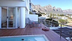 A modern hotel balcony with a pool, offering a view of mountains and a cityscape. - Holiday Apartment w Sea Views Pool CBT Suite (Cape Town)