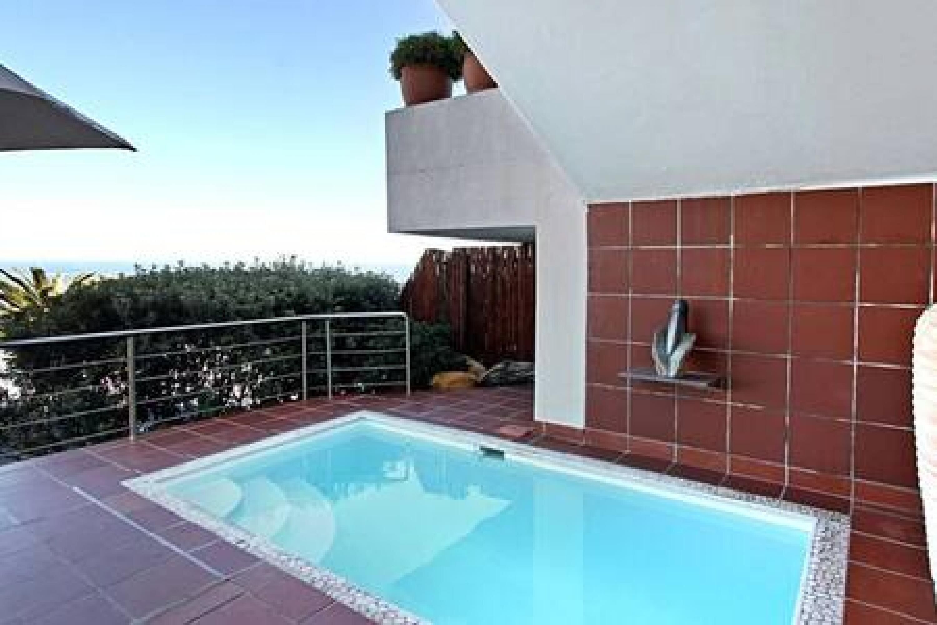A swimming pool with a tiled deck, a metal railing, and a view of the sea.