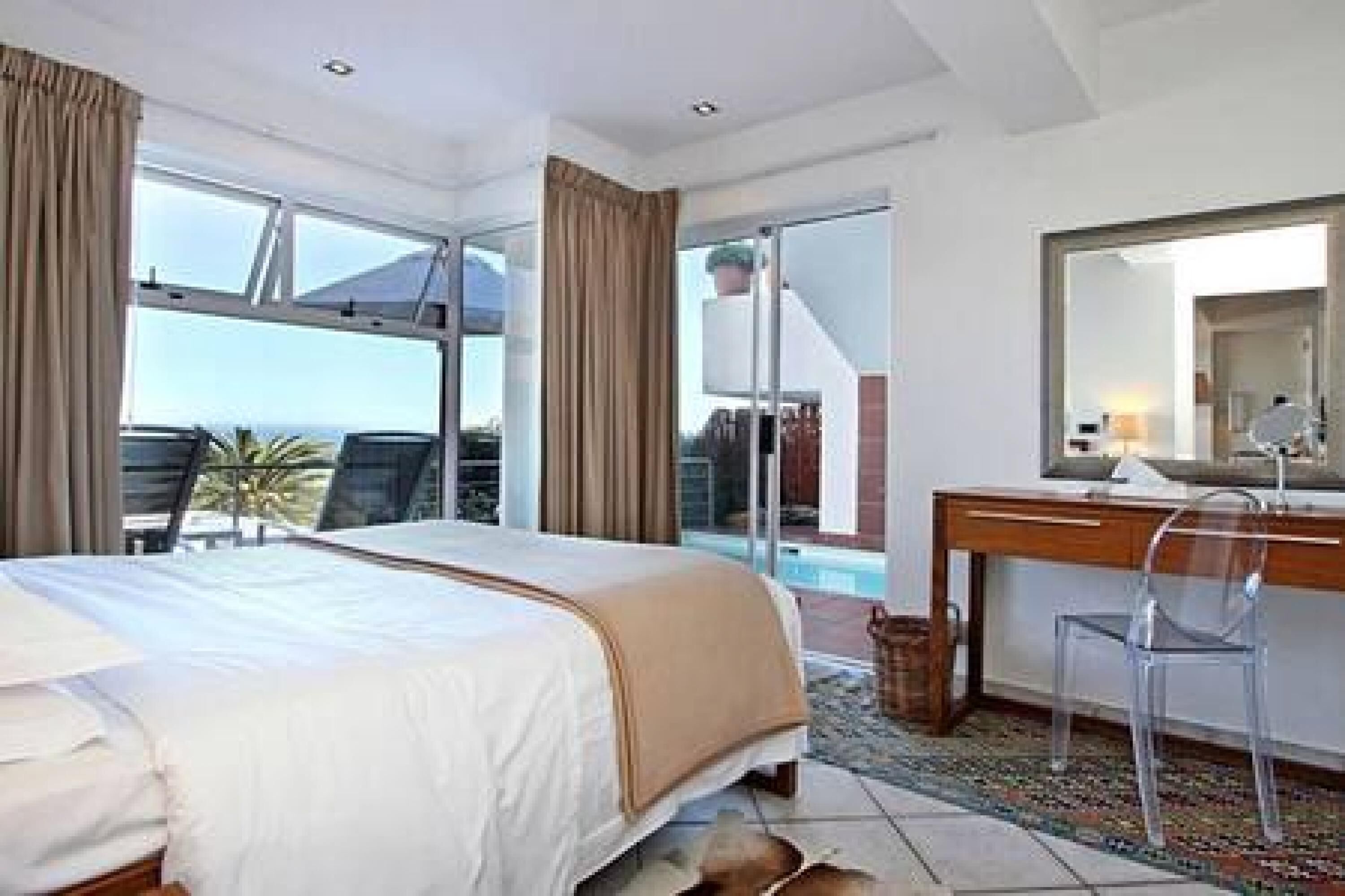 Habitación de hotel con cama, escritorio, silla, un espejo grande y vistas al exterior.