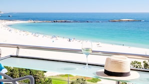 A balcony with a clear view of a beach, a glass of white wine, and a straw hat on the table. - Beautiful Holiday Apartment Overlooking the Beach Modoco (Cape Town)