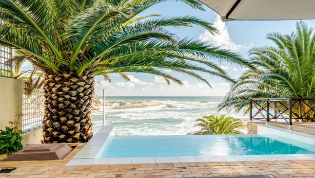 A pool area with a view of the ocean, palm trees, and a tiled deck. - Camps Bay Holiday Apartment w Private Pool CBT Palm Suite (Cape Town)
