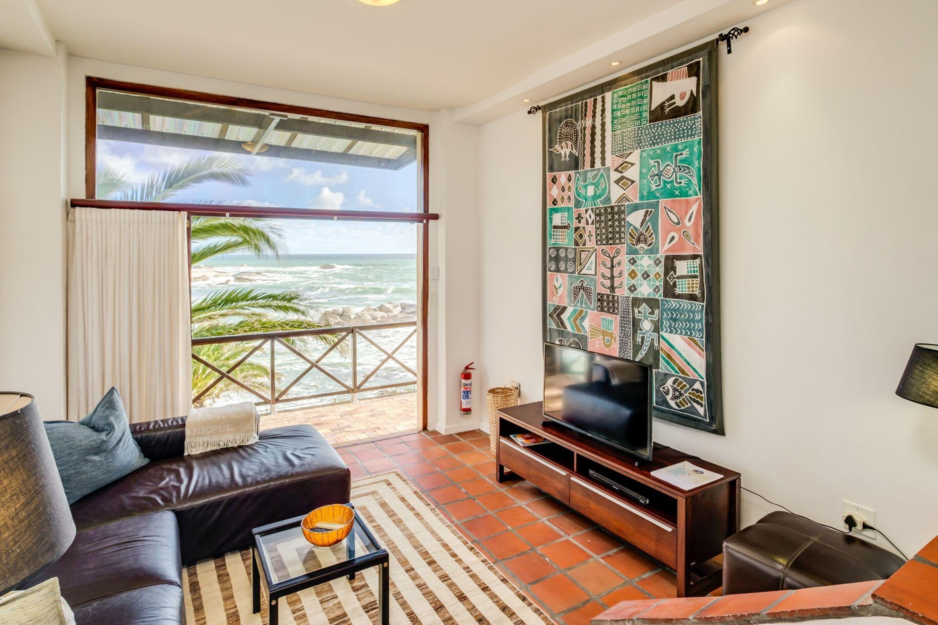 A living room with a large TV, a sofa, a coffee table, and a view of the ocean through a balcony.