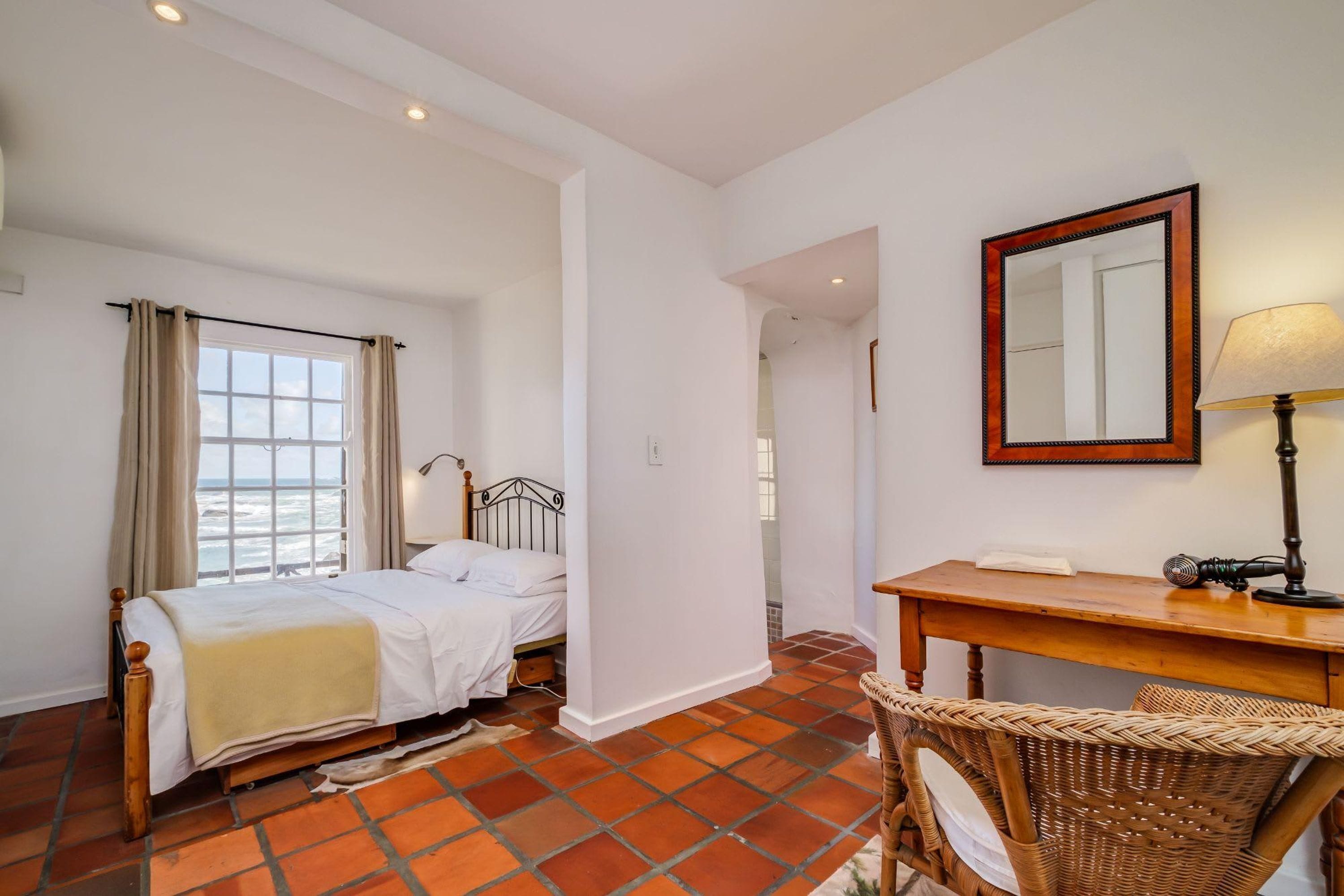 Ein Schlafzimmer mit Bett, Schreibtisch, Stuhl, Spiegel und Meerblick durch ein Fenster.