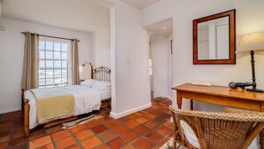 A bedroom with a bed, a desk, a chair, a mirror, and a view of the sea through a window. - Camps Bay Holiday Apartment w Private Pool CBT Palm Suite (Cape Town)