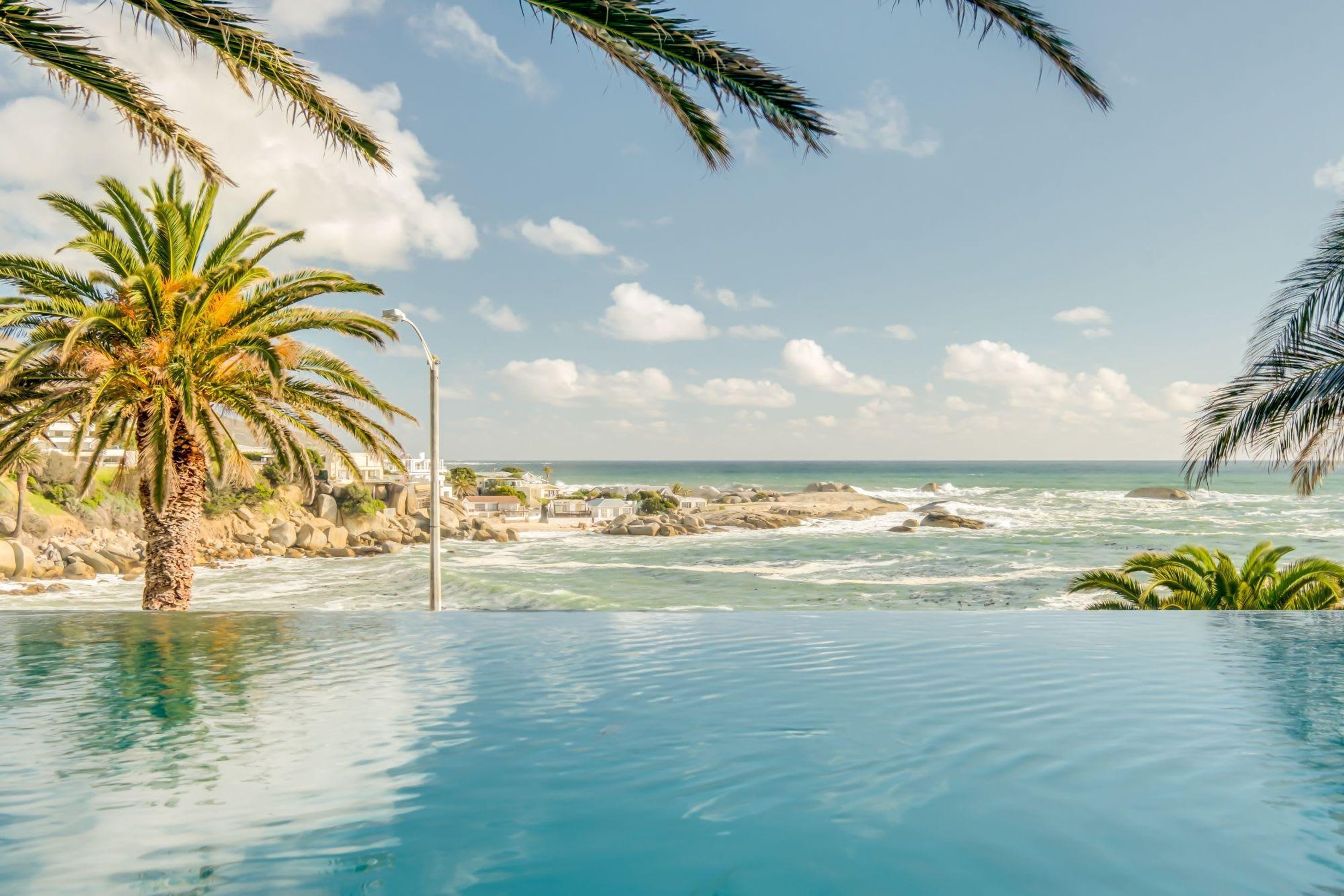 A poolside view with a clear ocean view, palm trees, and a rocky shoreline.