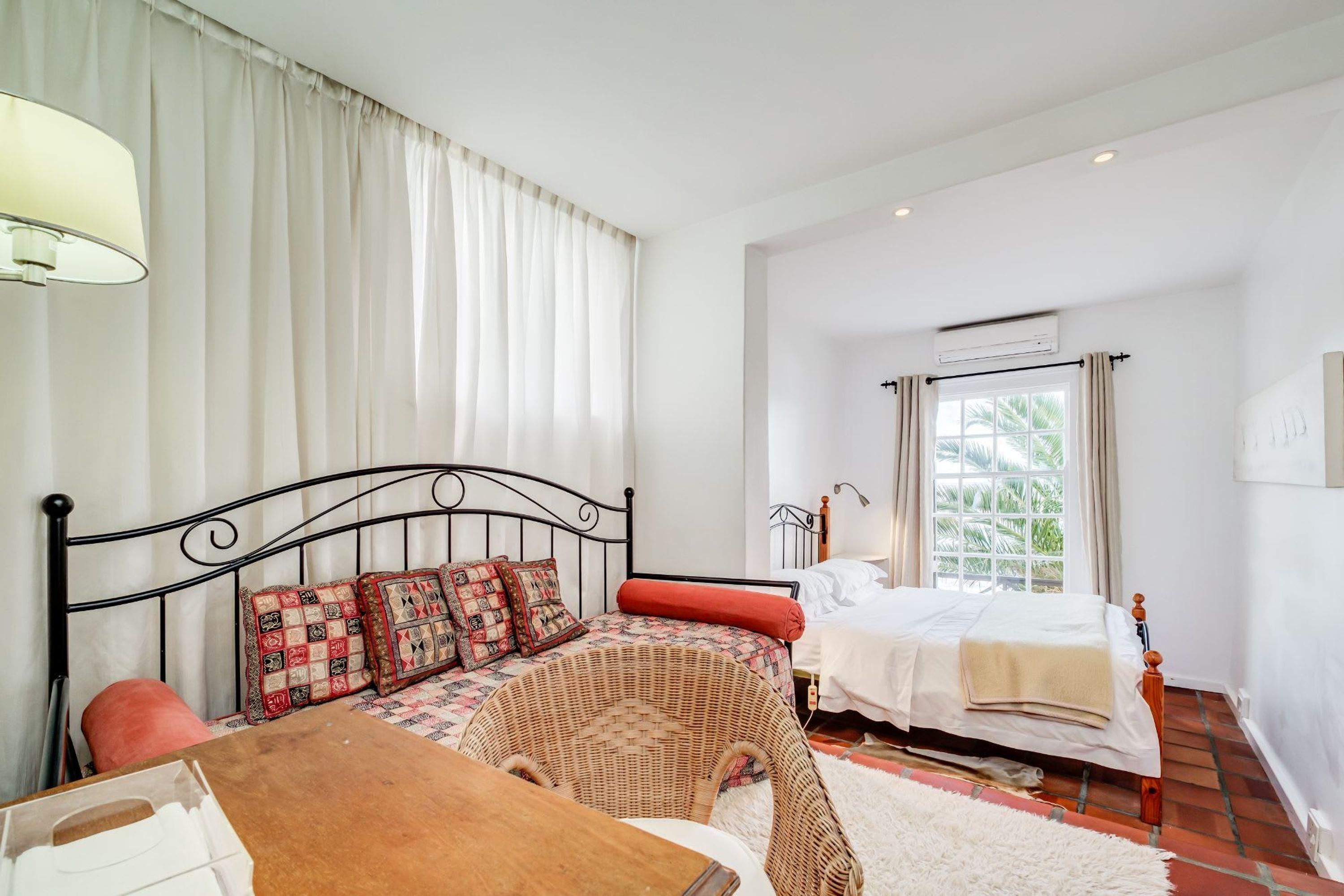 A bedroom with two beds, a wicker chair, a wooden table, and a white rug.