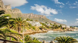 A coastal town with white buildings, palm trees, and a rocky cliff. - Camps Bay Holiday Apartment w Private Pool CBT Palm Suite (Cape Town)
