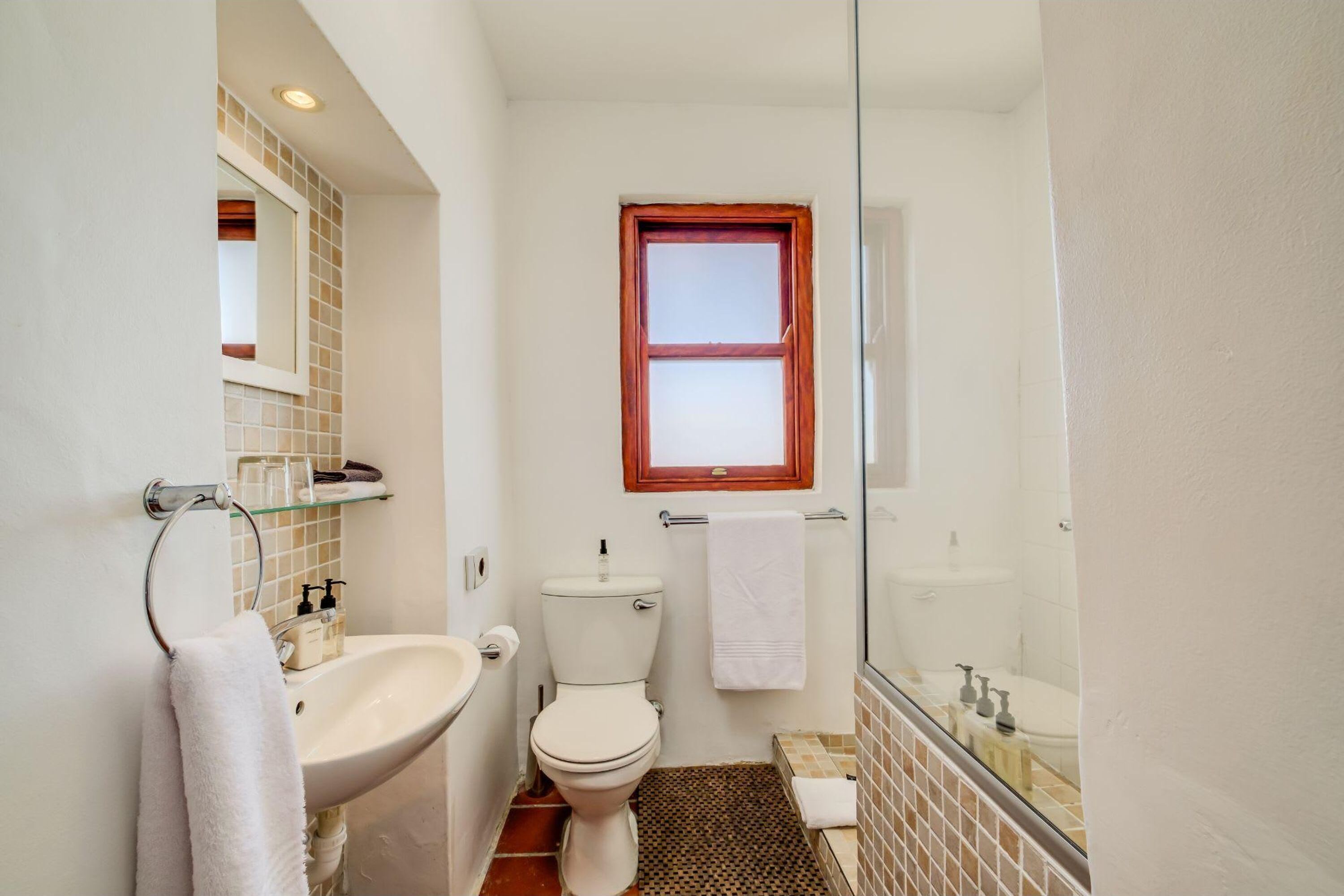 Een kleine badkamer met een wit wastafel, toilet en douchecabine met glazen wanden.
