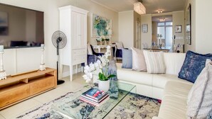 Ein modernes Wohnzimmer mit Flachbildfernseher, weißem Sofa, Glastisch und weißem Schrank.