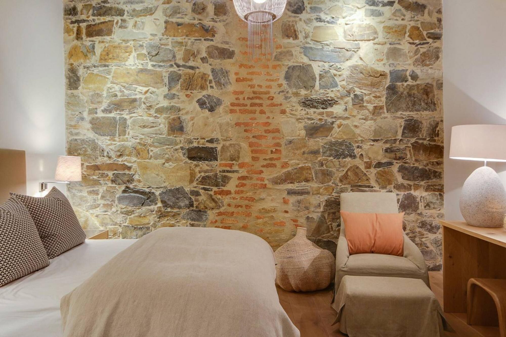 Una camera da letto con un muro in pietra, un letto, una sedia e una lampada.