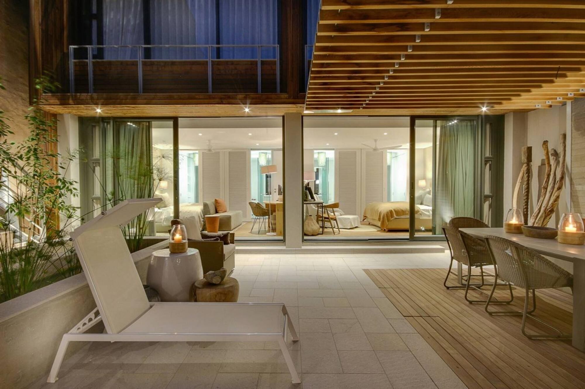 A modern interior with a lounge area, a dining space, and a bedroom visible through glass doors.