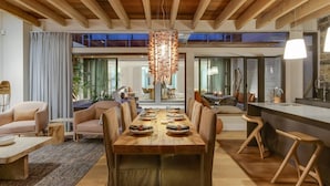 Een ruime eethoek met een houten tafel gedekt voor zes personen, omringd door moderne stoelen. Daarboven hangt een grote kroonluchter, en de ruimte heeft zichtbare houten balken in het plafond.