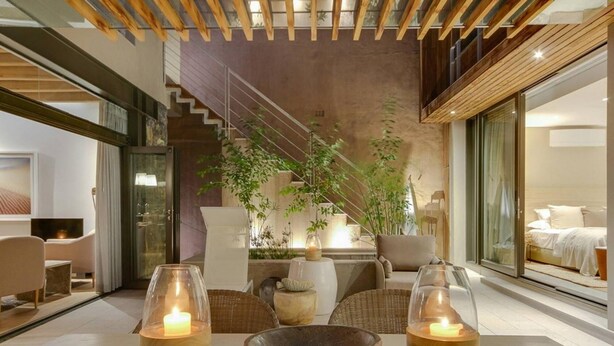 Een modern interieur met een eethoek, inclusief een tafel met drie kandelaars, een grote plant en een trap naar een hoger gelegen verdieping.