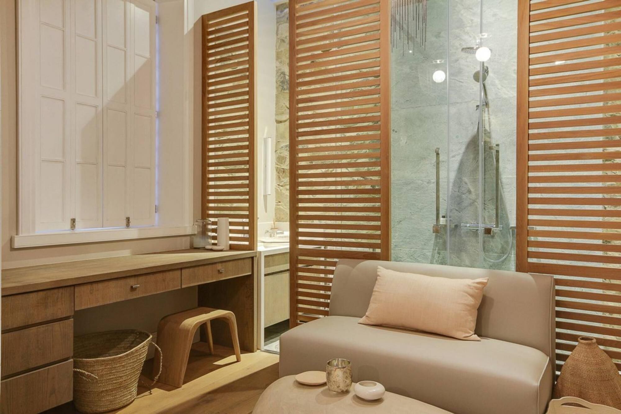 A modern bathroom with a wooden vanity, a glass shower enclosure, and a beige sofa with cushions.