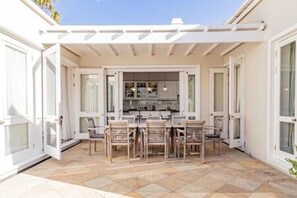 Un patio techado con una mesa y sillas de comedor, un área de cocina y una pared exterior blanca.