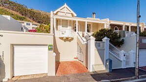 A two-story residential building with a white facade, a garage, and a staircase leading to the upper floor. - Lovely Holiday Home w Private Courtyard Six Selbourne (Cape Town)