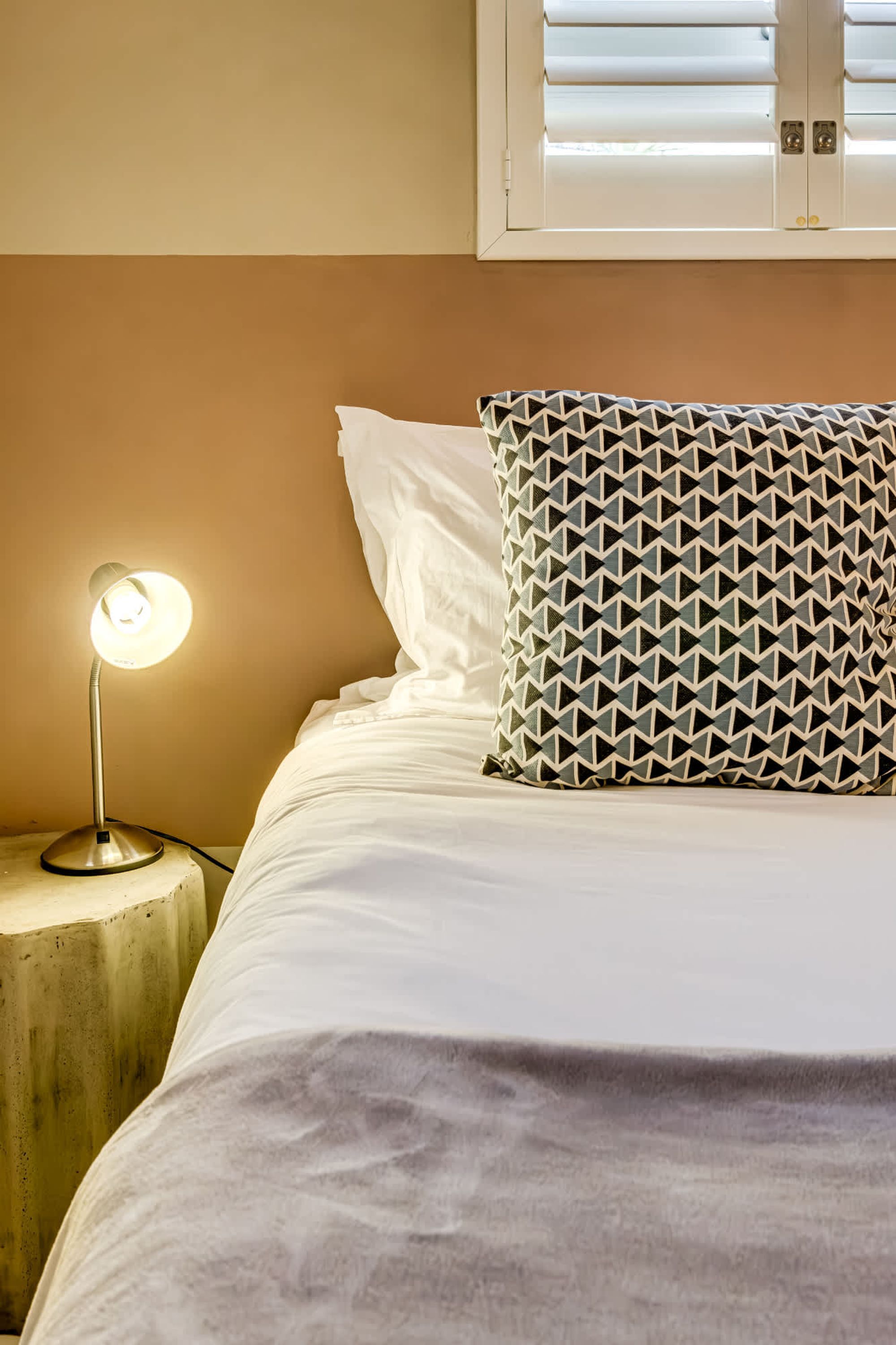 Un lit avec une literie blanche, un oreiller à motifs et une lampe de chevet.