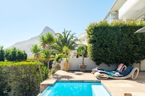 Área de piscina com espreguiçadeiras, um vaso de planta e montanhas ao fundo.