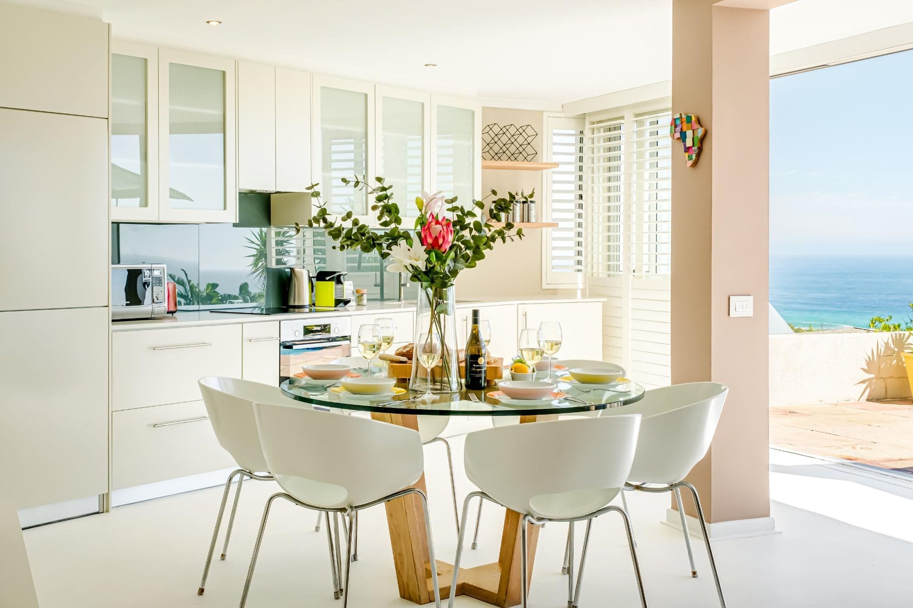 Een moderne keuken met een eetgedeelte, een glazen tafel en uitzicht op de oceaan.
