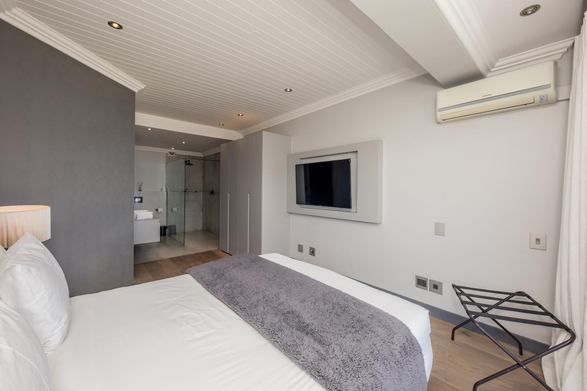 A modern hotel room with a large bed, a TV mounted on the wall, and a walk-in closet.