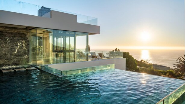A modern house with a glass infinity pool overlooking the ocean at sunset. - Spectacular Holiday Villa w Private Pool Gym Prima Views (Cape Town)