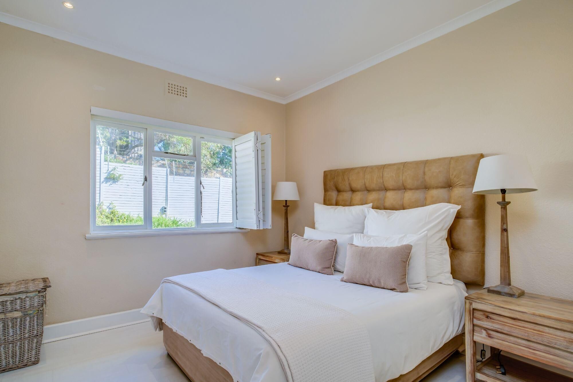 A bedroom with a large bed, two bedside tables, a window with curtains, and a view of the outside.